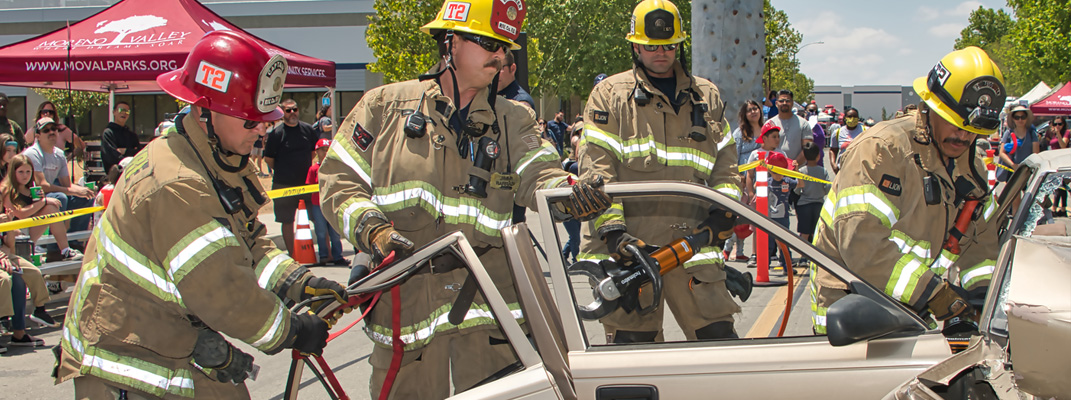 Four firemen doing a rescue demonstration on a car.